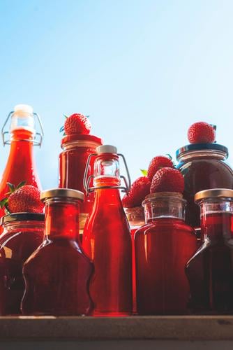 Glass bottles and jars with strawberries syrup and jam containers delicious dessert food fresh fruit syrup fruits full glass bottle glass vessels