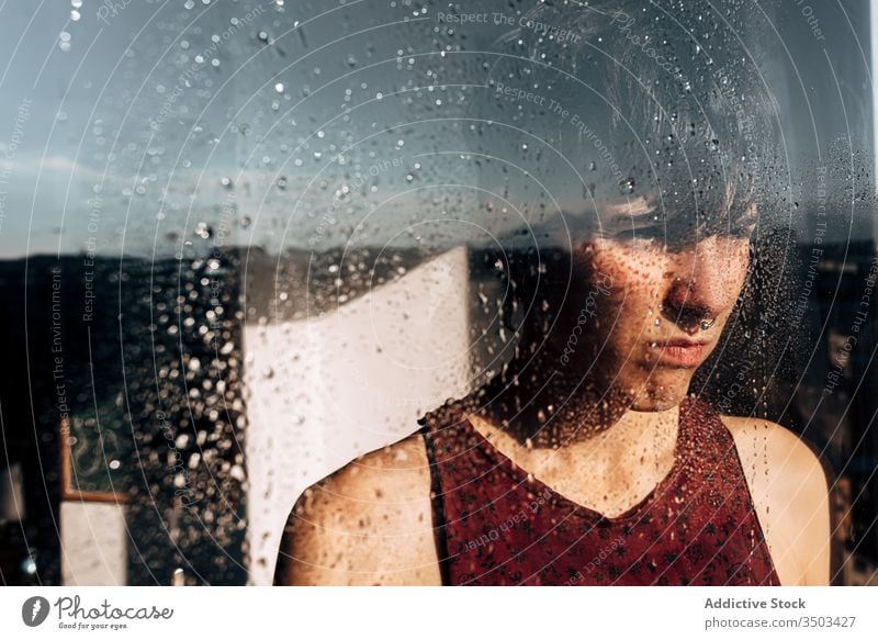 Unhappy woman looking through window at home sad lonely unhappy melancholy pensive depression isolation coronavirus young female wet solitude stress frustrate
