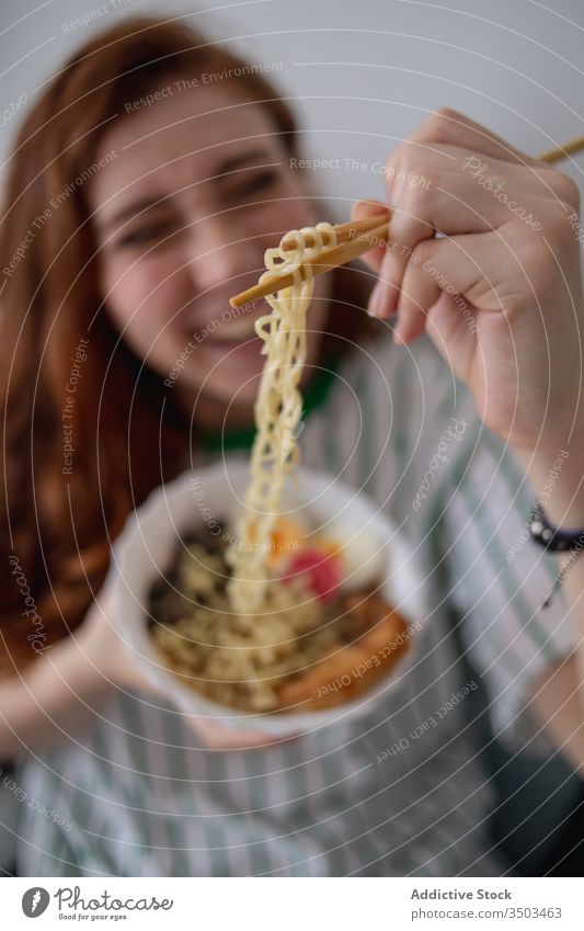 Happy woman eating noodles at home ramen happy japanese sofa chopstick young female redhead cheerful food tradition authentic asian oriental laugh couch tasty