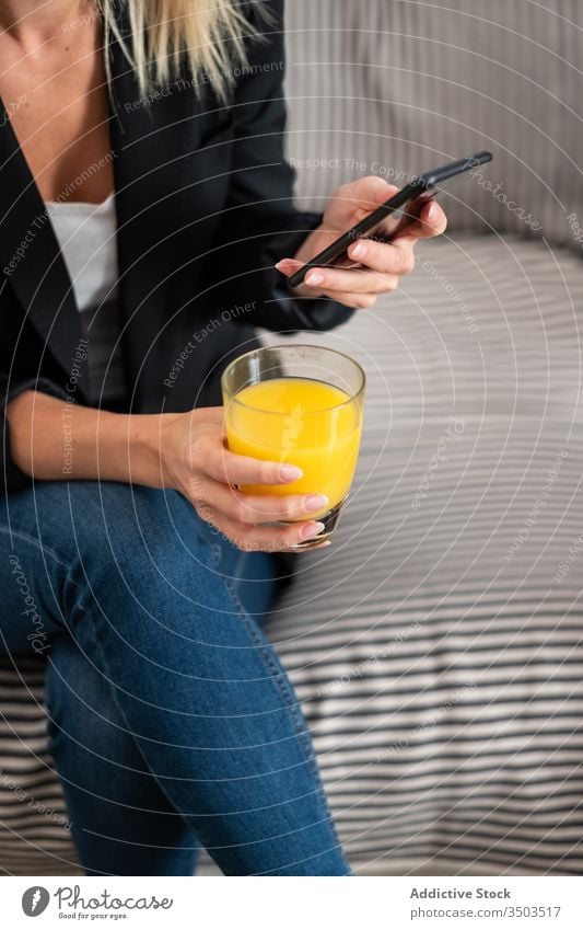 Anonymous woman drinking juice and using smartphone on sofa home mobile phone rest female social media lounge healthy sit fresh orange browsing couch glass