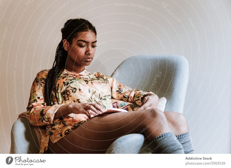 Ethnic woman with book resting at home read african american black casual chair brunette calm sitting young cozy ethnic piercing free time relax lifestyle