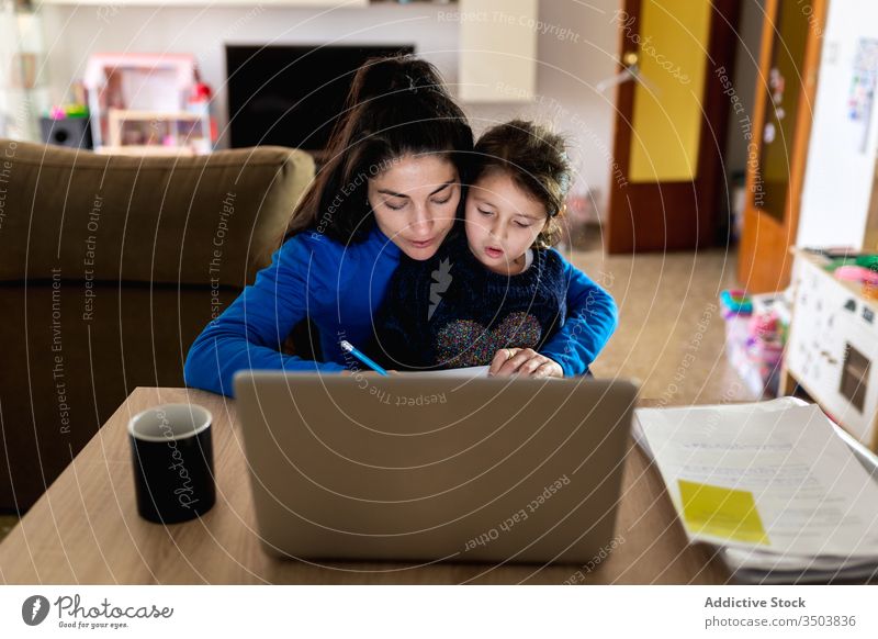 Mother with daughter working on remote project mother freelance home hug read paper laptop table woman girl busy child kid together device gadget document