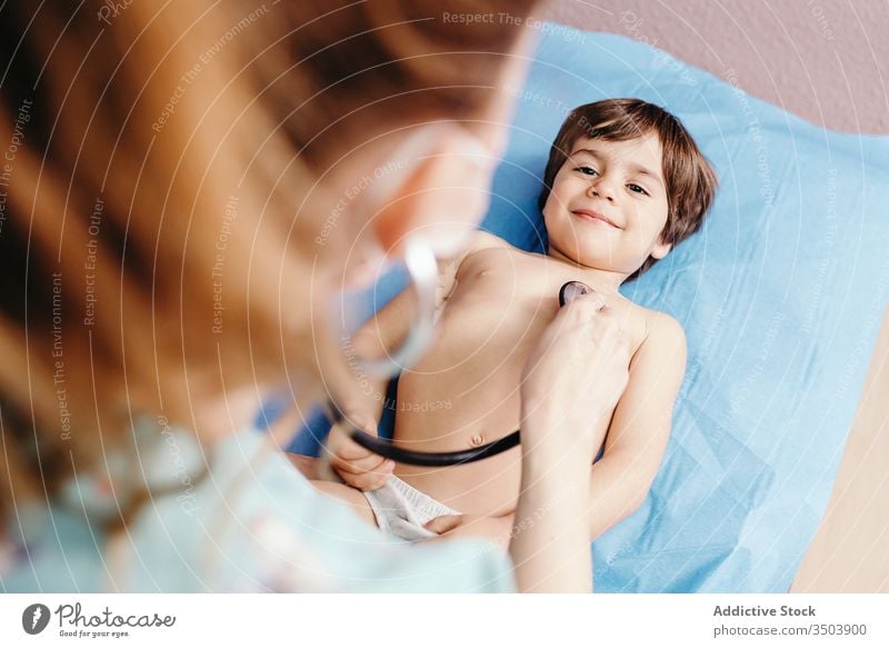 Doctor with stethoscope examining kid in clinic doctor examine cheerful smile hospital little boy lying couch chest respiratory patient health care medicine