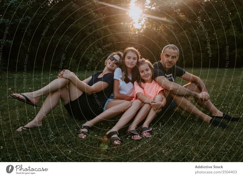 Happy family resting on green meadow together nature relax sit park forest countryside summer smile active casual grass love relationship lifestyle tree bonding