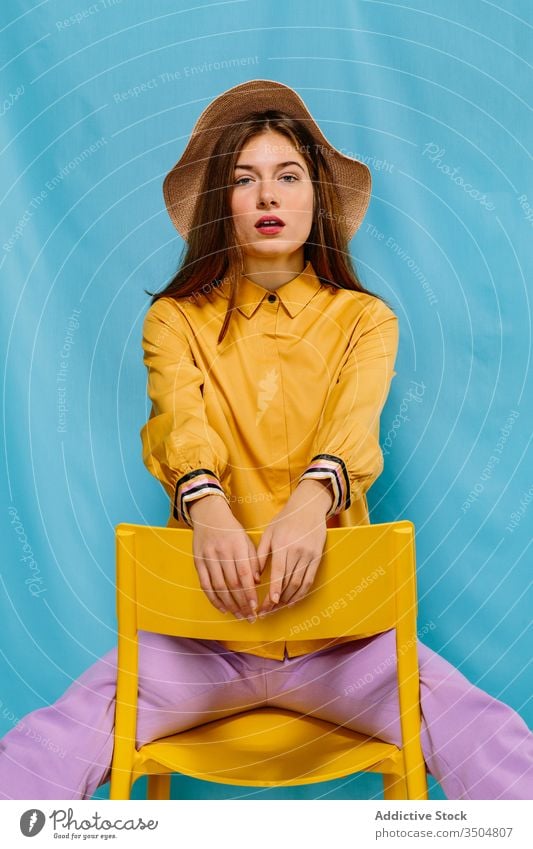 Stylish female model sitting on chair woman trendy style colorful outfit young fashion confident hat summer sensual urban millennial chill serious individuality