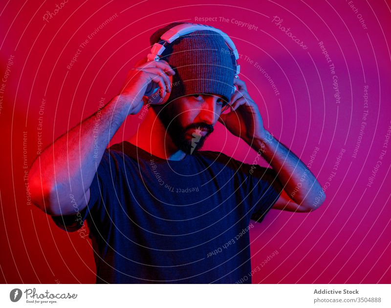 Bearded man listening to music in headphones style modern beard red light bright nightlife male illuminate neon device vibrant gadget sound casual hat entertain