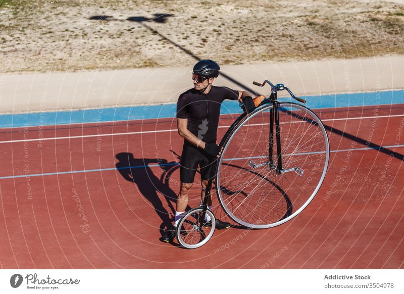 Thoughtful adult sportsman with high wheel bike at sports stadium bicycle cyclist penny farthing sports ground fit rider workout athlete sporty determine