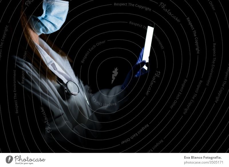doctor woman indoors, using mobile phone. Wearing protective gloves, mask and stethoscope. coronavirus covid-19 concept internet tecgnology dark corna virus