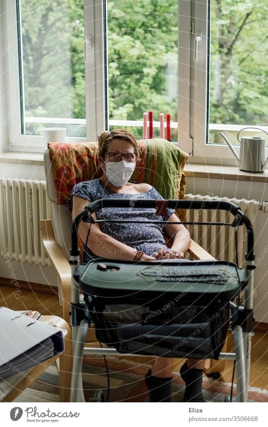 Woman in the risk group with mask and rollator sits alone at home in isolation due to the corona crisis Risk group covid-19 insulation Mask handicapped