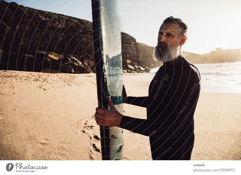 senior man with long beard carrying surfboard at beach men vacation surfing adult standing grey hair lifestyle holding sport hobby portrait ocean waves