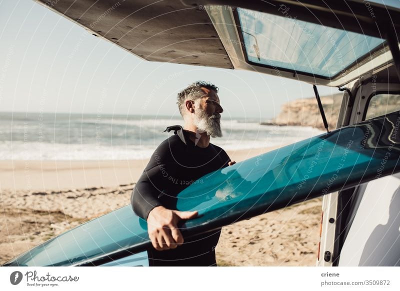Senior man taking surfboard out of van at beach senior men transport trip vacation surfing adult beard grey hair lifestyle joy hobby