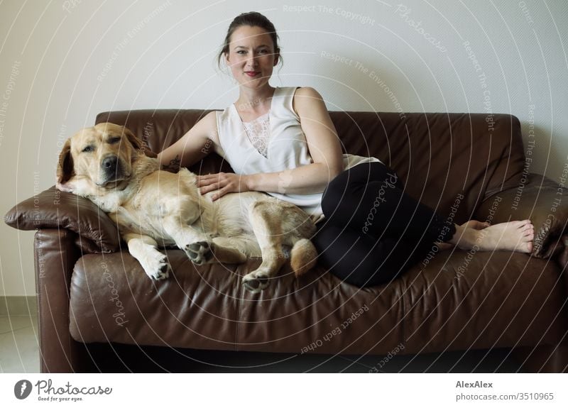 Blond Labrador and young woman sitting on a brown leather couch Pet Dog Blonde Cute is sits Young woman Youth (Young adults) 18 - 30 years Leather Interior shot
