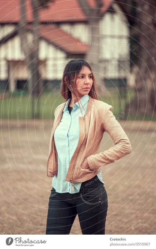 Woman standing on the street with her hands in a leather jacket facing away vertical portrait woman young girl female feminine house building park nature autumn
