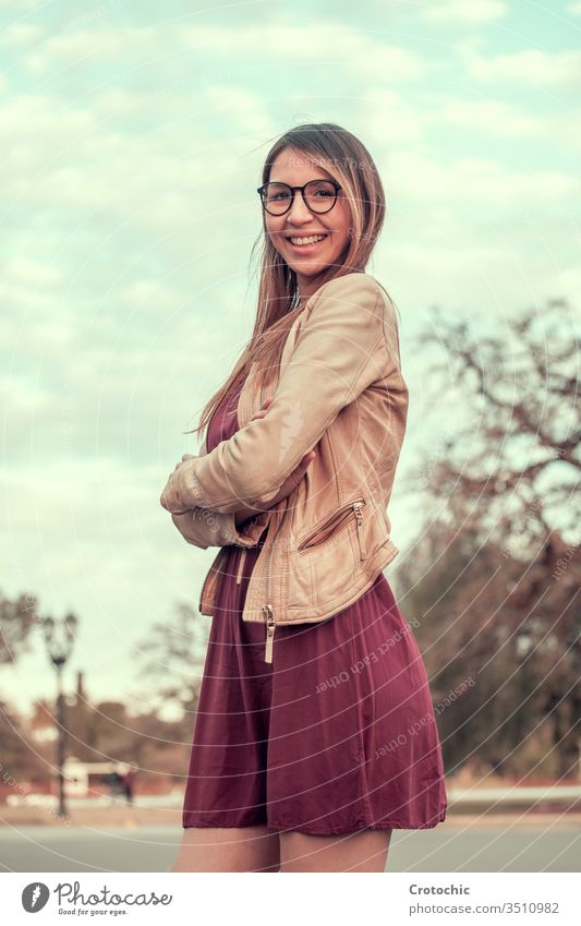 Portrait photo of a girl with long hair and glasses in a purple dress in a park vertical portrait smile expression face turn elegant woman young female feminine