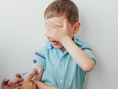 Little boy is afraid to vaccinate little vaccine caucasian injection kid white covered eyes blue shirt hand during vaccination children concept pediatrician