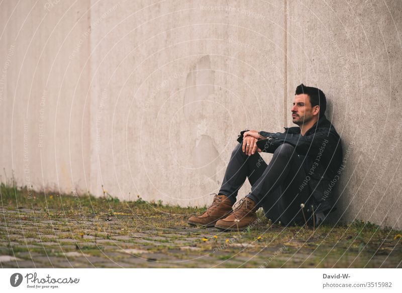 Man sits lonely on a wall Lonely Wall (building) out by oneself Meditative frustrated Frustration Copy Space top Copy Space left Copy Space middle Model