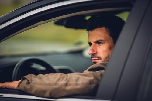 Man sits in car and looks seriously out the window Earnest view outside Rear view mirror Mirror look back Road traffic Car Window Open Exasperated Sour Evil