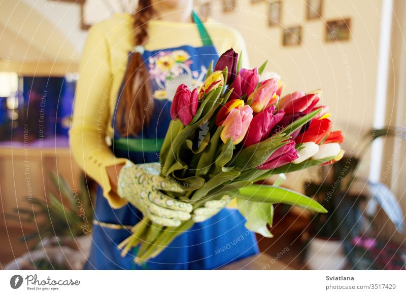 The seller holds a large beautiful bouquet of tulips packed. Side wiev hands paper kind pink packaging floral market scissors spring gloves ribbons rope
