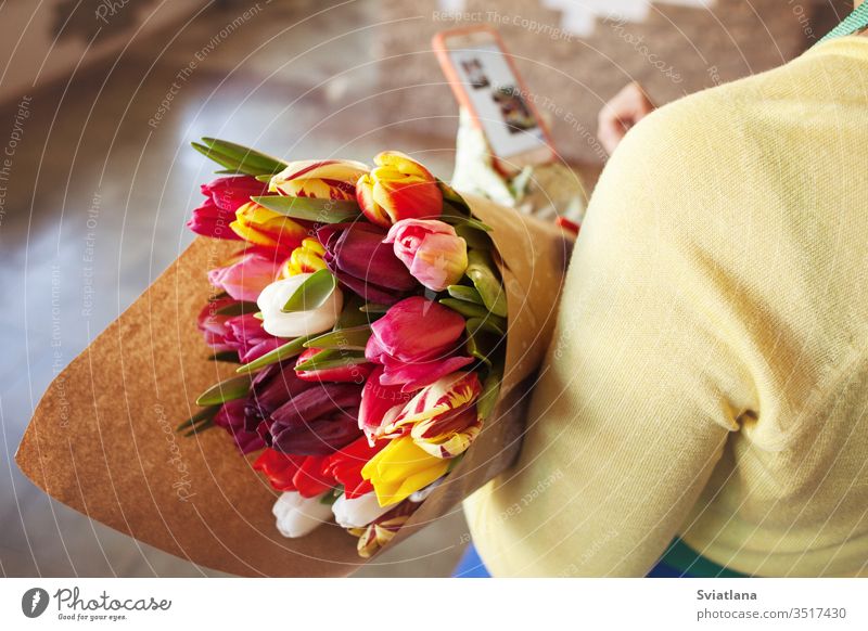 The seller holds a large beautiful bouquet of tulips packed in craft paper. Top view hands kind pink packaging floral market scissors spring gloves ribbons rope