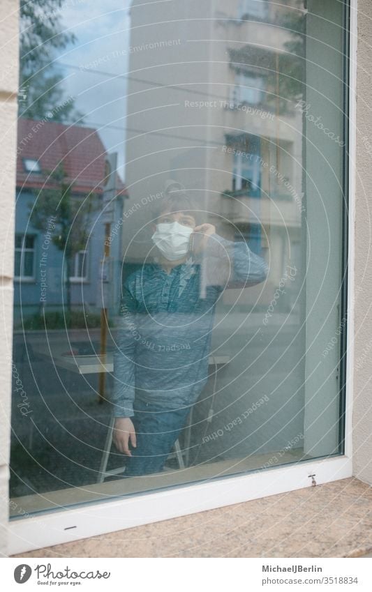 Boy with mouth-nose-protection mask stands at the window and makes a phone call during contact ban due to coronavirus pandemic in Germany Boy (child) Child Mask