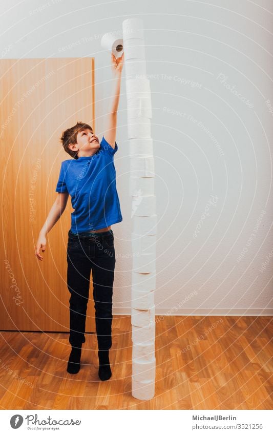 Boy balances piles of toilet paper left Stack Toilet paper Balance Boredom Boy (child) challenge Child Corona covid-19 Epidemic game Tall Hoarders Hoarding Home