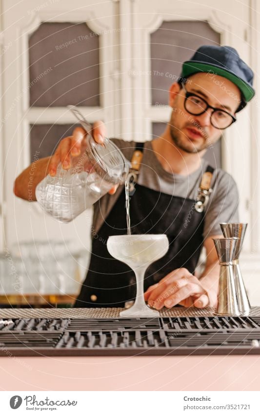 Vertical photo of a waiter transferring liquid into a glass with ice to a frost cocktail glass alcohol bar pouring glasses mint apron hotel fresh restaurant