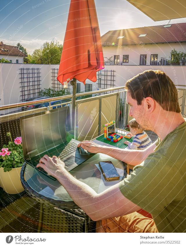 Home Office, father and son are working together with their laptops at home at the balcony, while the sun is shining. New lifestyle caused by corona, covid-19 pandemic.