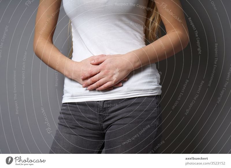 unrecognizable young woman holding her stomach with both hands - concept for abdominal pain, irritable bowel syndrome, bellyor stomach ache, painful periods or menstrual cramps