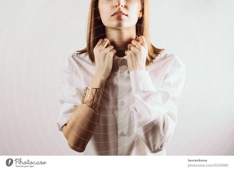 Portrait of young adult woman holding collar of white shirt with her hands, selective focus rings faceless jewelry studio bracelet lady portrait hair caucasian