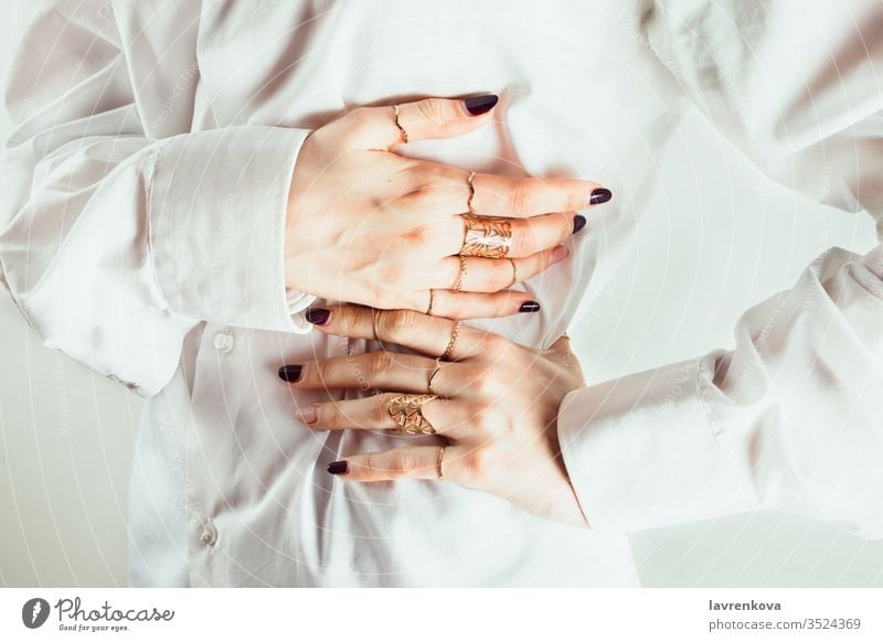 Closeup of white woman's hands with various rings around her waits, white shirt, white background, selective focus. gesture decor luxury jewelry