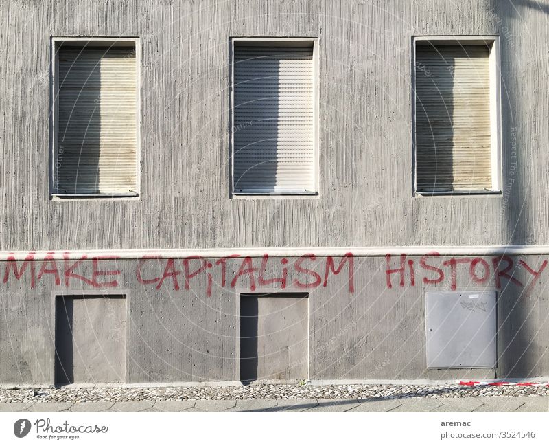 Grey house wall with closed shutters and inscription Gray Capitalism Make capitalism history Criticism Facade saying slogan Wall (building) Deserted