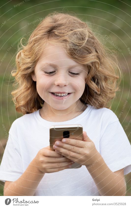Funny child with long hair holding a mobile phone park leisure cellphone childhood smartphone lifestyle boy blond communication connection casual clothing