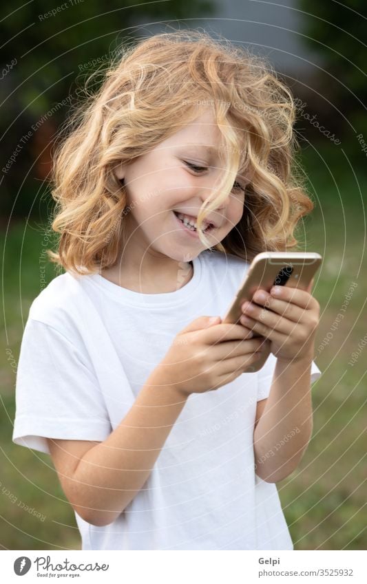 Funny child with long hair holding a mobile phone park leisure cellphone childhood smartphone lifestyle boy blond communication connection casual clothing