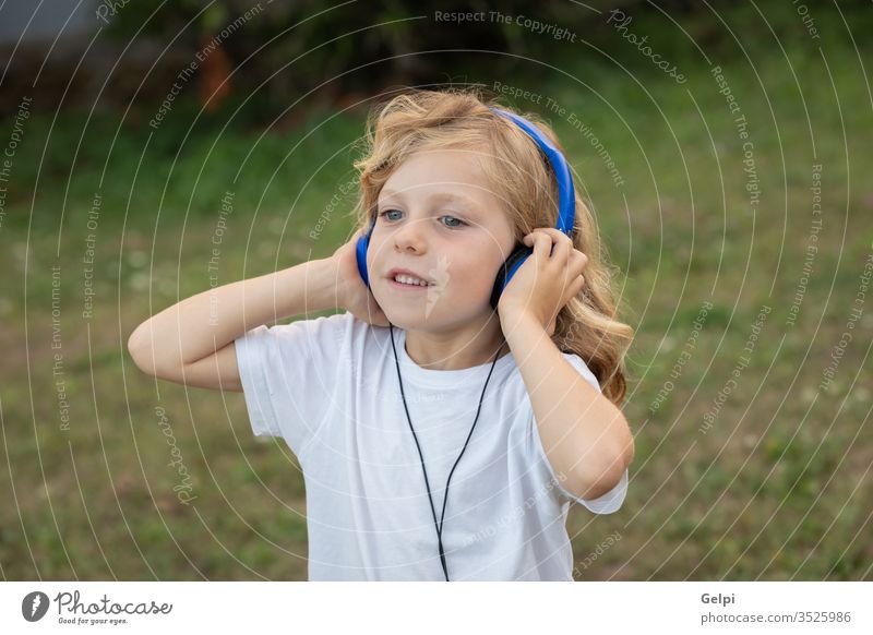 Funny child with long hair listening music with blue hadphones park childhood kid joyful headphones fun blond healthy person happiness earphones happy young