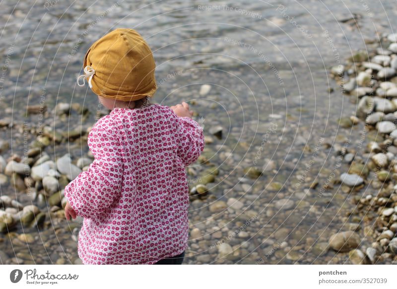 Female toddler playing with stones at the riverbed Toddler Playing Water River Isar Throw garments sun protection Hat Yellow Flowery pattern spring Summer