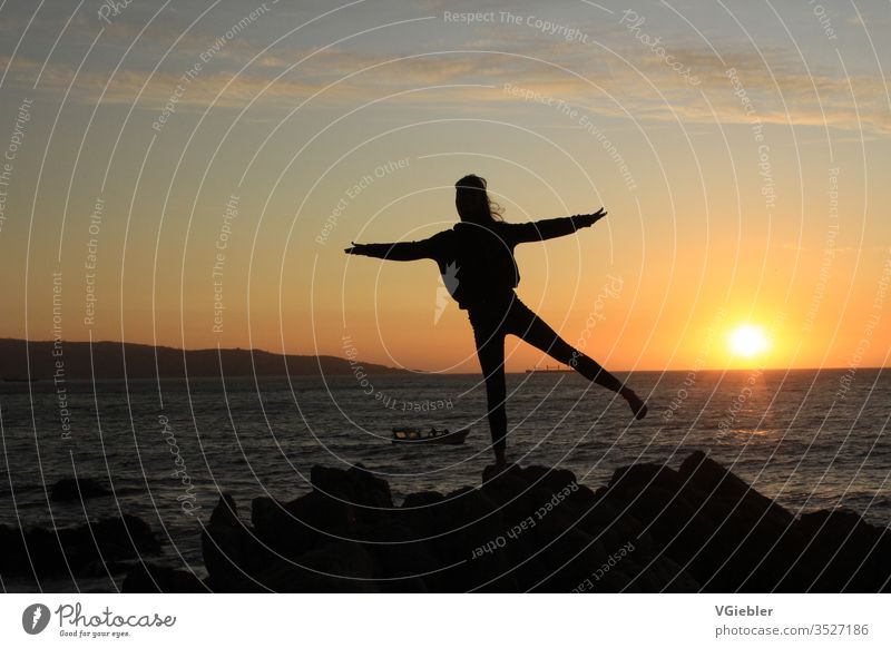 Outline of a girl before sunset, standing on a rocky ground, in the background the sea and a boat Coast sihouette luck Joy Sky Sun Summer Action Calm Sunset