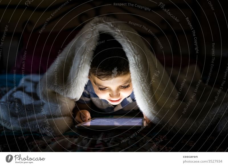 Little child using a tablet covered with a blanket alone application bed bedroom bedtime boy childhood children only children playing communication computer