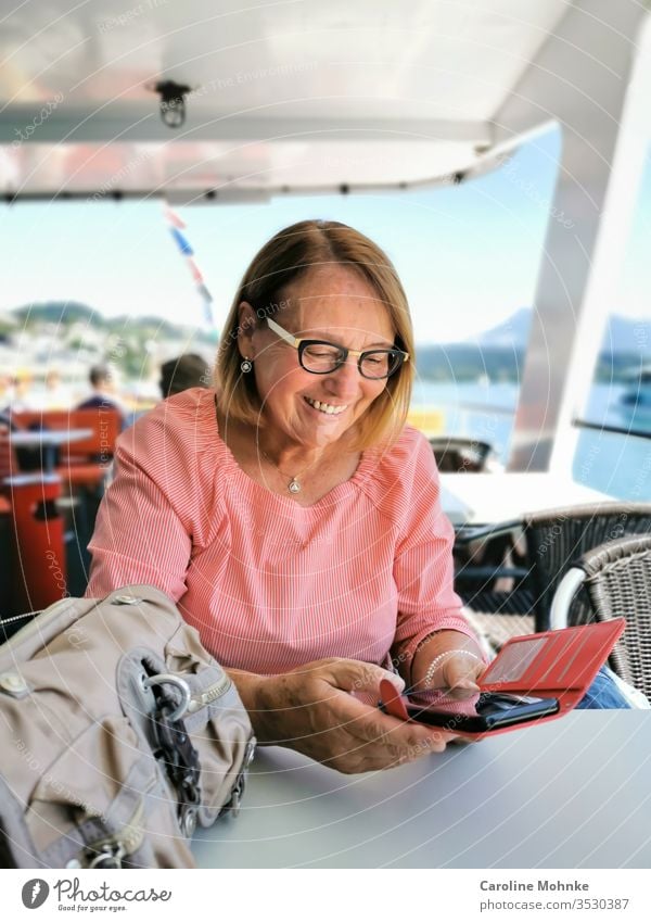 Ü70 Woman checking joyful messages on her smartphone during a cruise Senior citizen joyfully retired pensioner Navigation ship Boating trip Laughter Mode