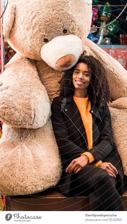 Happy ethnic woman sitting with giant teddy bear happy positive cheerful smile toy plush big female african american coat young lifestyle joy relax black