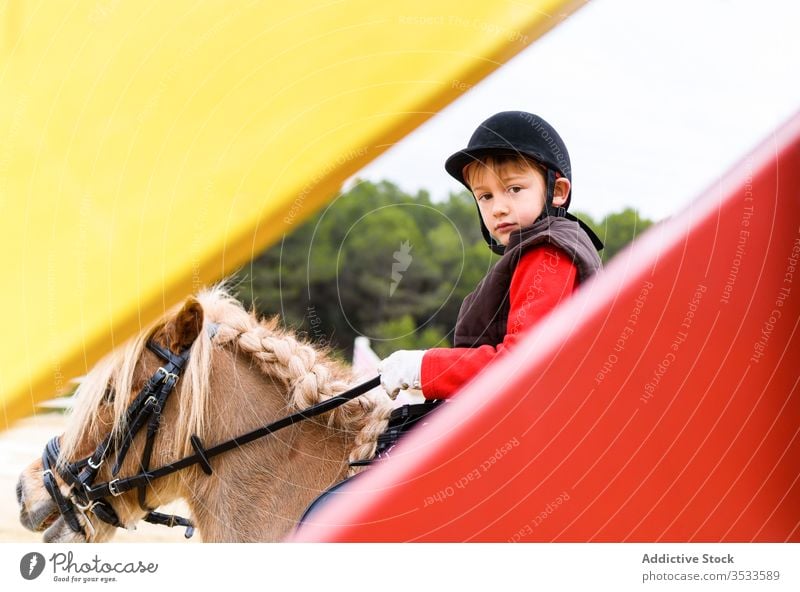 Boy riding pony behind barrier boy ride jockey arena dressage lesson school equestrian helmet kid child uniform safety protect mane braid horseback animal sport