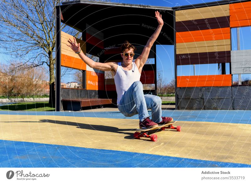 Young man falling from skateboard ride trick sports ground hipster arm raised urban city male skater street energy hobby sunny modern activity practice