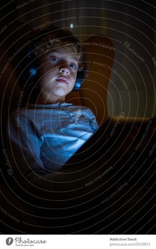 Vertical picture of a child sitting looking at a tablet with headphones at night with a distracted look boy imagination cinema multimedia communication listen