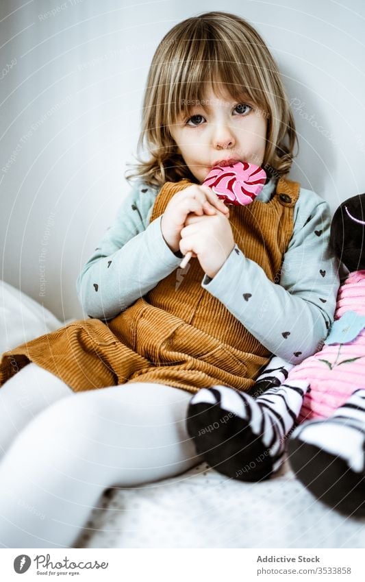 Little girl eating candy on bed lollipop suck home toy sit rest cute little bedroom child kid plush sweet childhood soft cozy innocent relax casual lifestyle