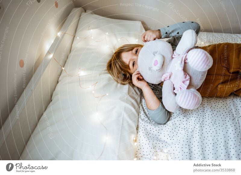 Happy girl playing on soft bed happy toy hug laugh fairy light plush lying excited child kid love garland bedroom little childhood lifestyle leisure fun cute