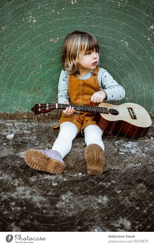 Girl with ukulele sitting near shabby wall girl music kick scooter play casual little rough ground weathered green child street kid building grunge instrument