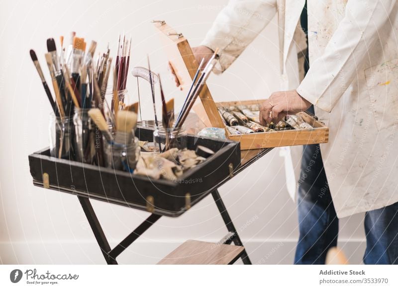 Senior artist standing in home workshop and choosing paints man aged set paintbrush choose concentrate studio hobby gallery equipment modern table design