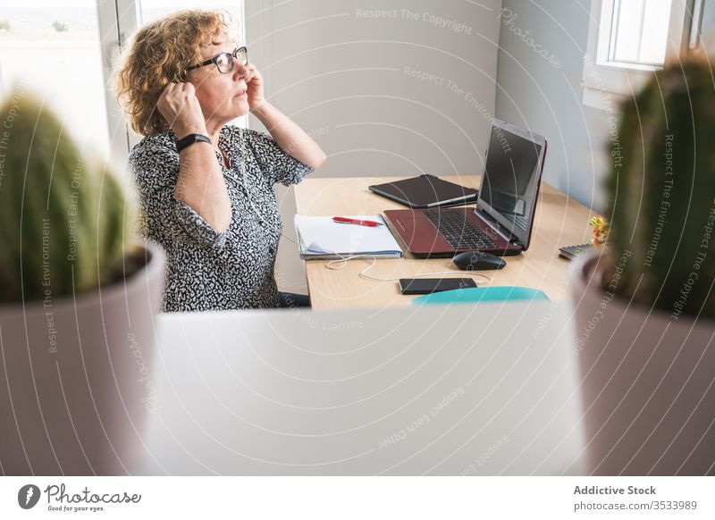 Adult woman working on laptop in room decorated with cactuses in pots plant using freelance home earphones internet remote distance business computer netbook