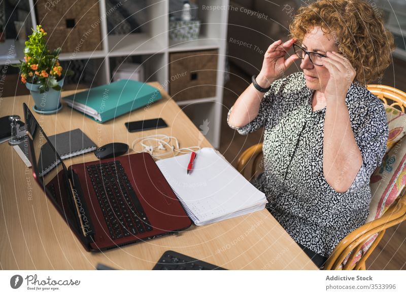 Thoughtful adult woman listening music in earphones while working on laptop at home rest distance remote break enjoy notebook eyes closed using freelance relax