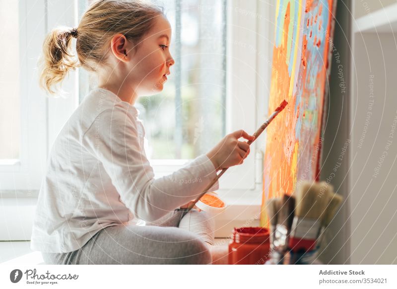 Little girl painting picture with paintbrush canvas draw rainbow creative colorful orange sill casual window art hobby imagination bright sit indoors