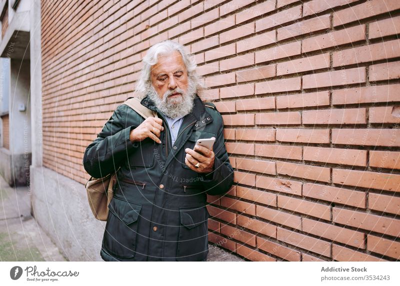 Male hipster using mobile phone on a brick wall senior man smartphone city serious street male elderly aged leaning gray hair long hair masculine handsome
